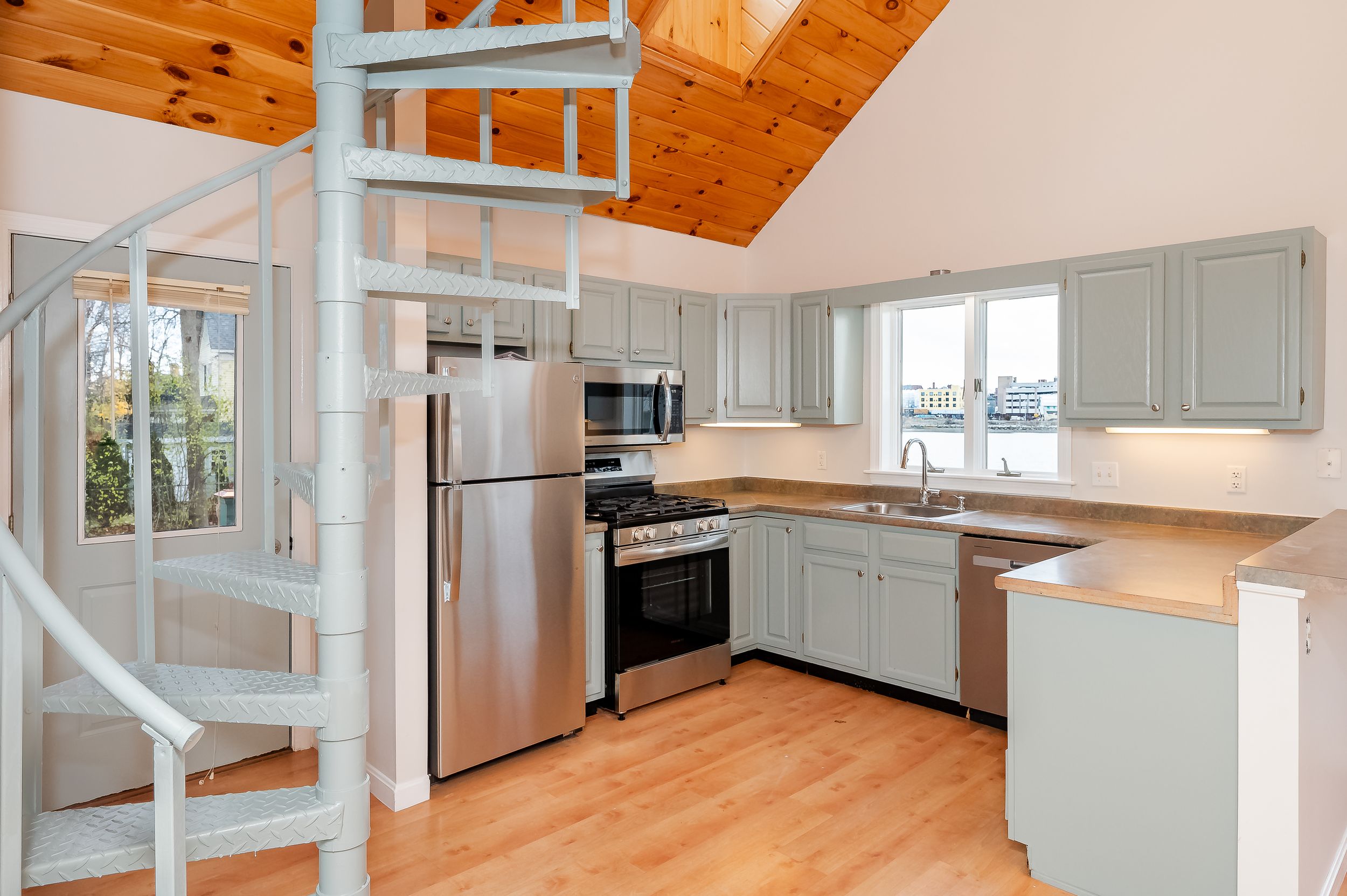 Modern kitchen with light gray cabinets, wood ceiling, stainless appliances and hardwood floors in an open floor plan.