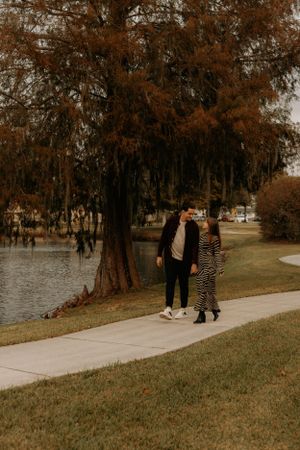 Two people stroll together on a concrete pathway beside a lake with fall foliage.