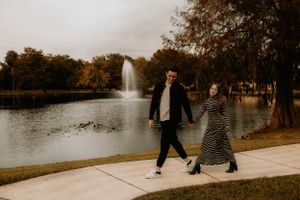 People walking along a scenic park path with a fountain and lake view.