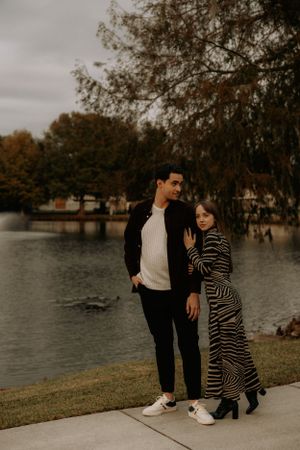 A couple in casual attire enjoys an autumn walk by the water.