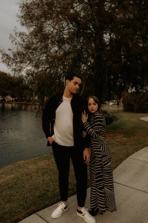 Two people in contrasting outfits share a moment by the lake.