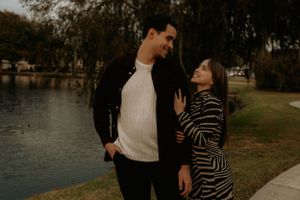 A couple poses together on a path near a lake during golden hour.