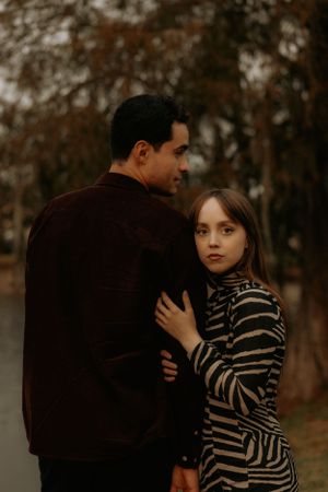 A romantic couple embraces in a moody autumn setting with dark trees in the background.