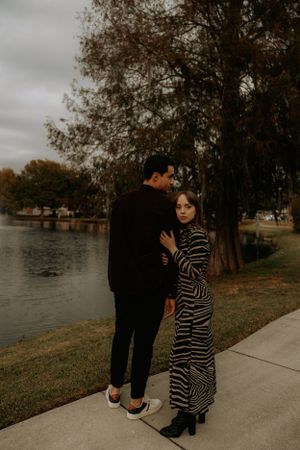 Couple standing together on a pathway near a lake during golden hour.