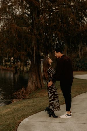 Two people share an intimate moment on a sidewalk surrounded by autumn trees.