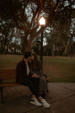 Couple sitting close together on a park bench at dusk.