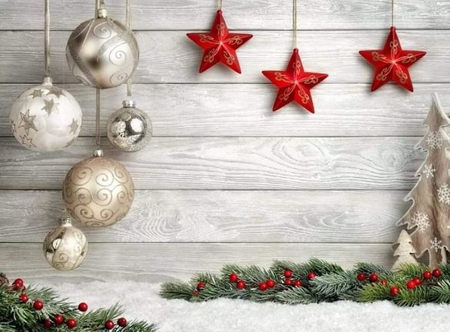 Silver Christmas ornaments and red stars hanging against a white wooden background with pine garland.