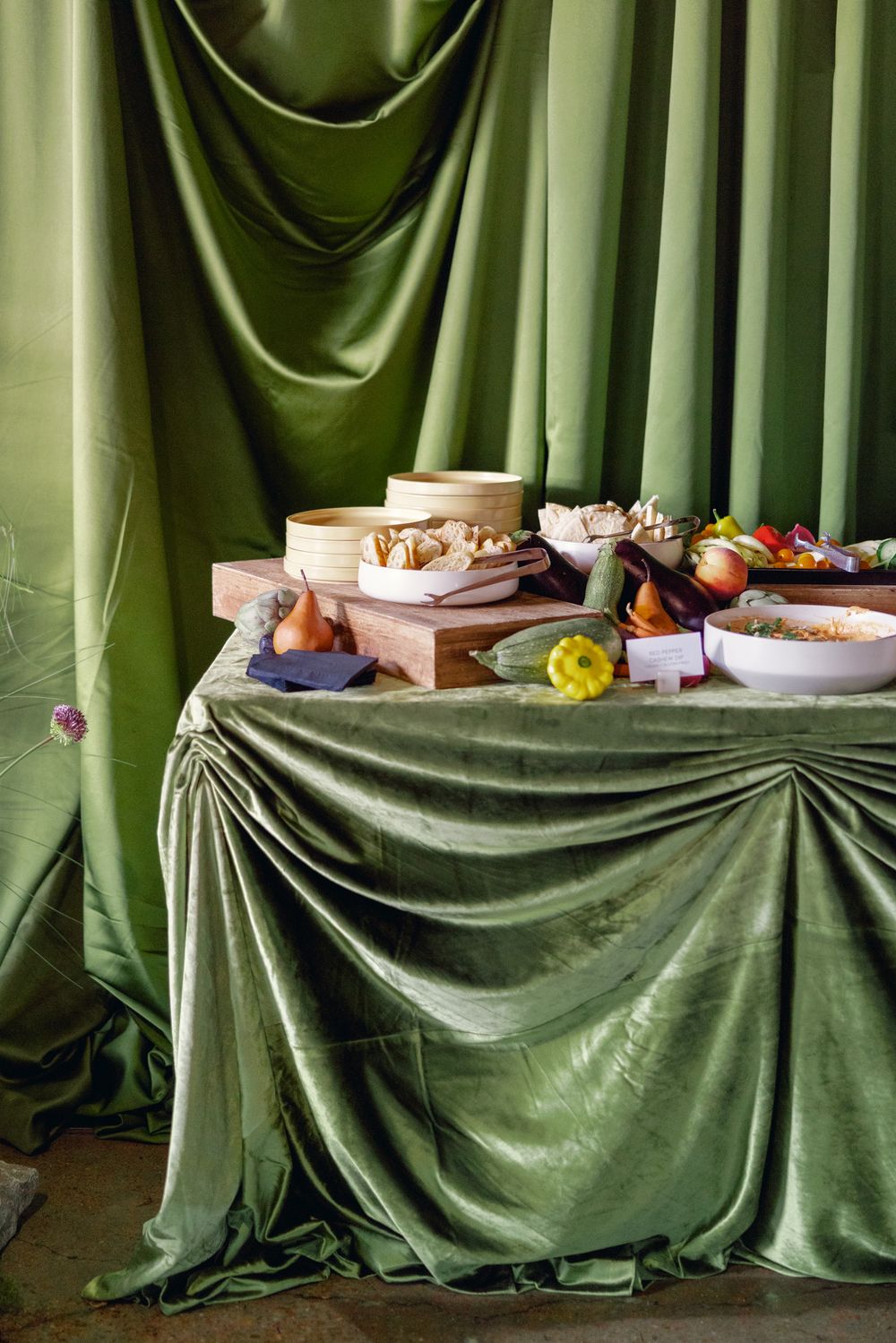 Still life scene with food and dishes arranged on a table draped with luxurious green velvet fabric.