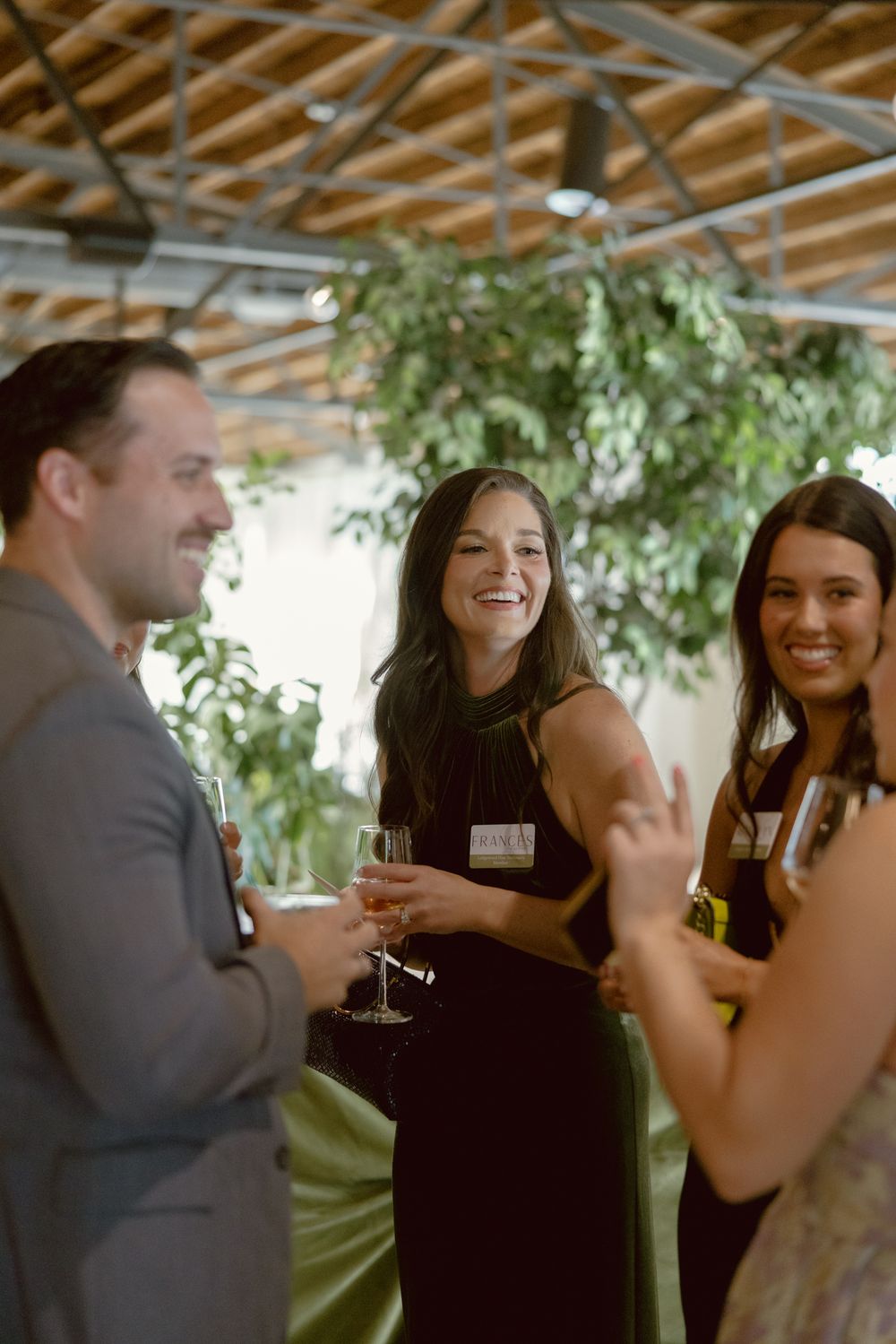 A group of party guests share laughter and conversation while enjoying drinks at an indoor event.