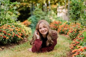 Cheerful teenage girl lying in grass surrounded by vibrant orange flowers in garden.