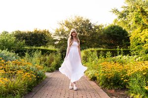 A brick pathway winds through a vibrant summer garden filled with yellow flowers and lush greenery.