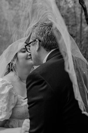 Black and white intimate portrait of a couple sharing a kiss under a wedding veil.