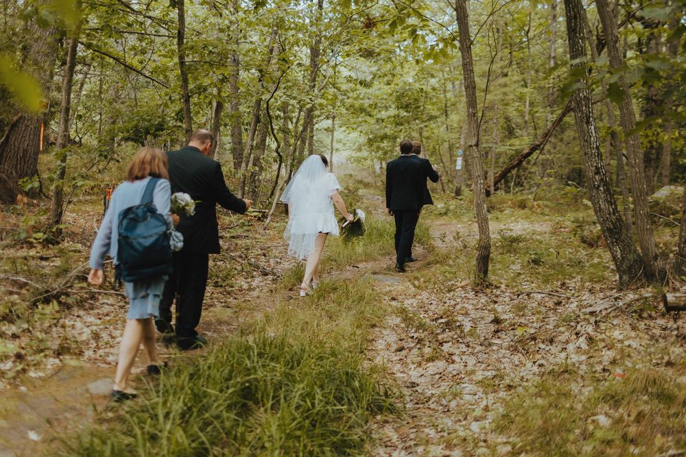 People walking through a wooded area with fallen leaves on the ground.