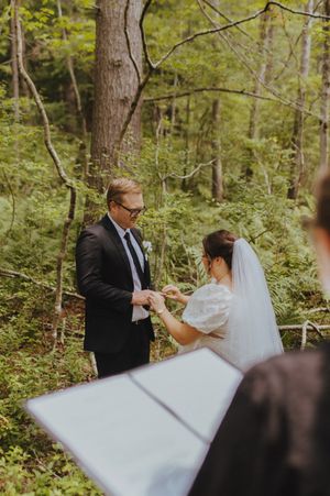A couple exchanges rings during their wedding ceremony in a wooded forest setting.