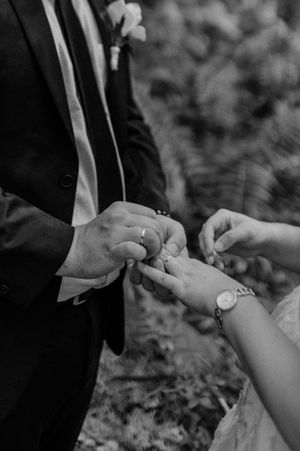Close-up black and white shot of hands exchanging wedding rings during a ceremony.