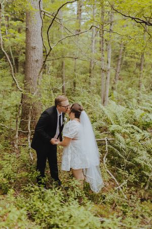 A couple shares an intimate moment during their forest wedding ceremony surrounded by ferns.