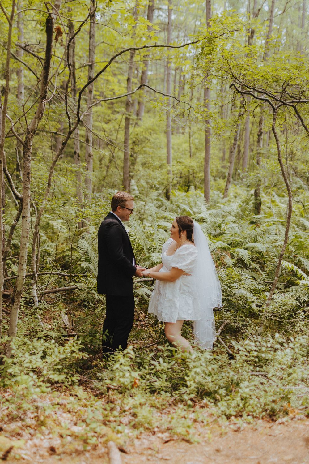 Wedding ceremony taking place in a lush forest setting with ferns and trees.
