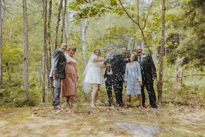 Wedding party poses for a celebratory photo with confetti in a forest setting.