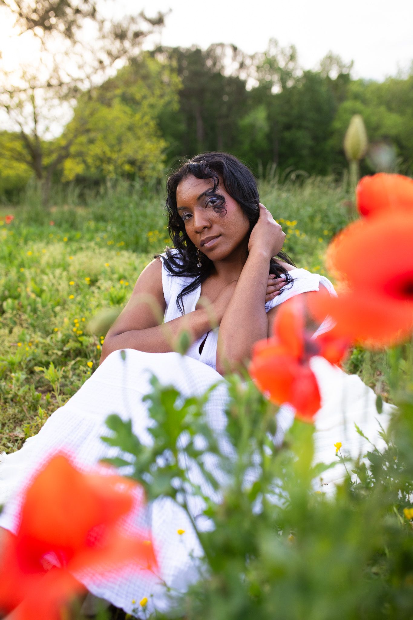 A dreamy outdoor portrait in a meadow with vibrant red poppies in the foreground and lush greenery behind at Juniper Creek Farm