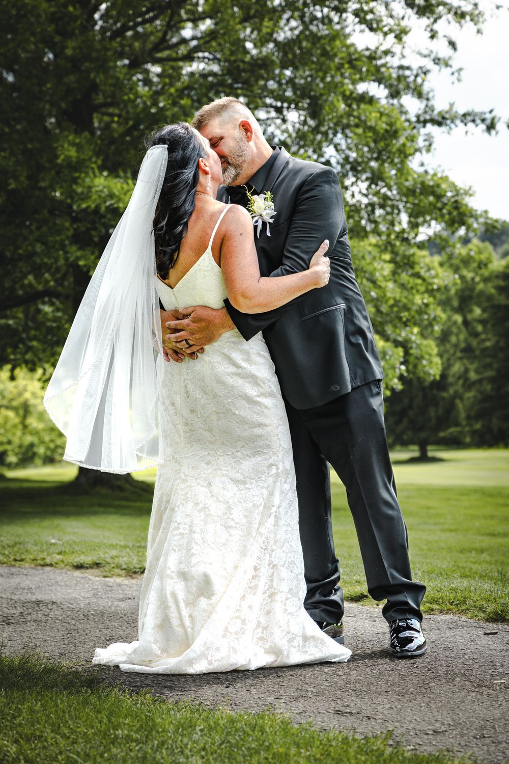 A romantic wedding moment captured on a gravel path with lush green scenery in the background.