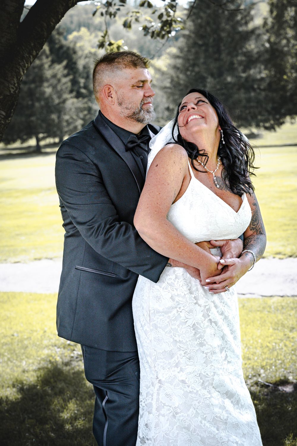 Romantic wedding couple embraces in a sunlit garden setting wearing formal attire.