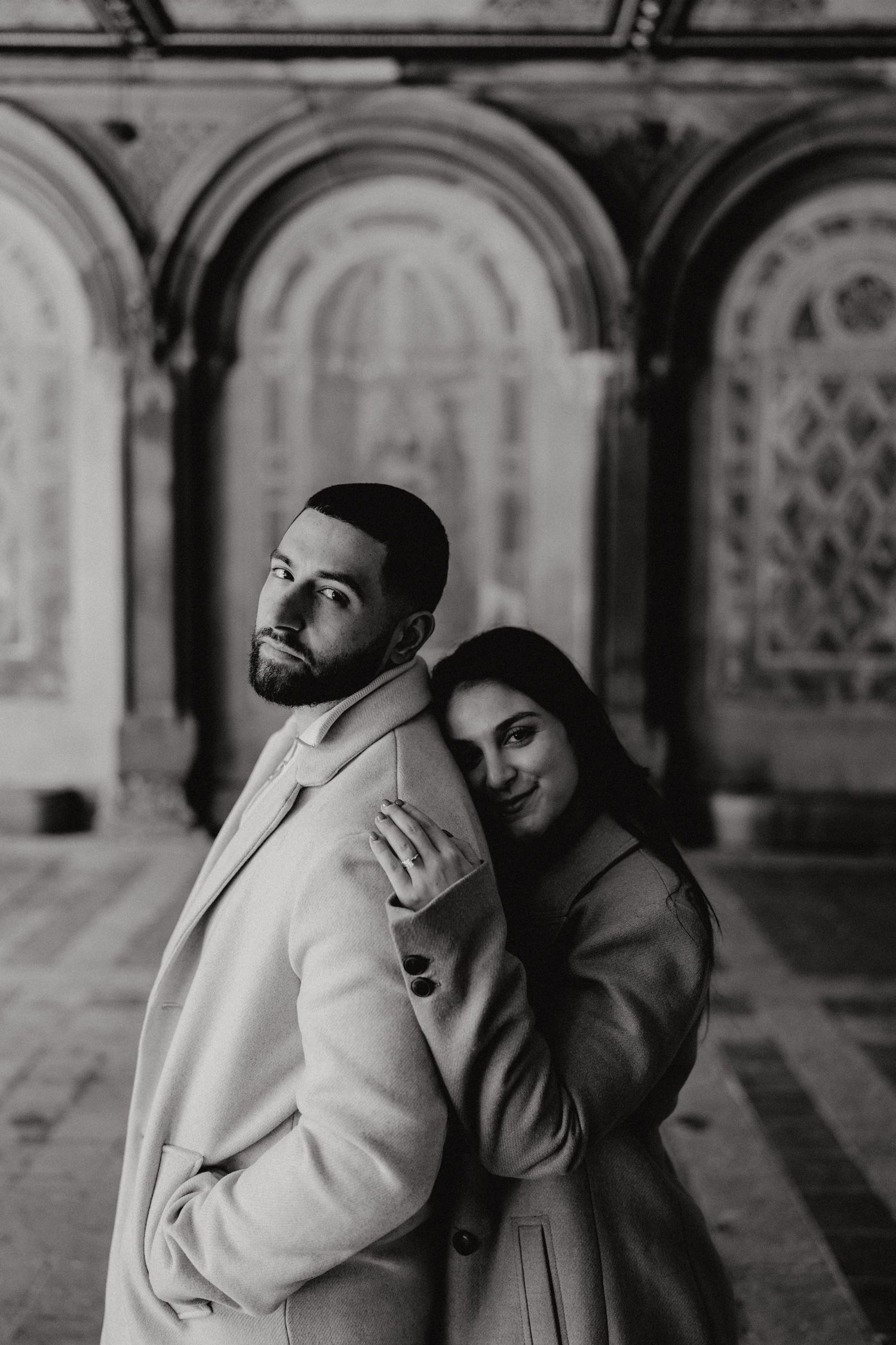 A stylish couple posing dramatically against the Bethesda Terrace arches in winter coats.
