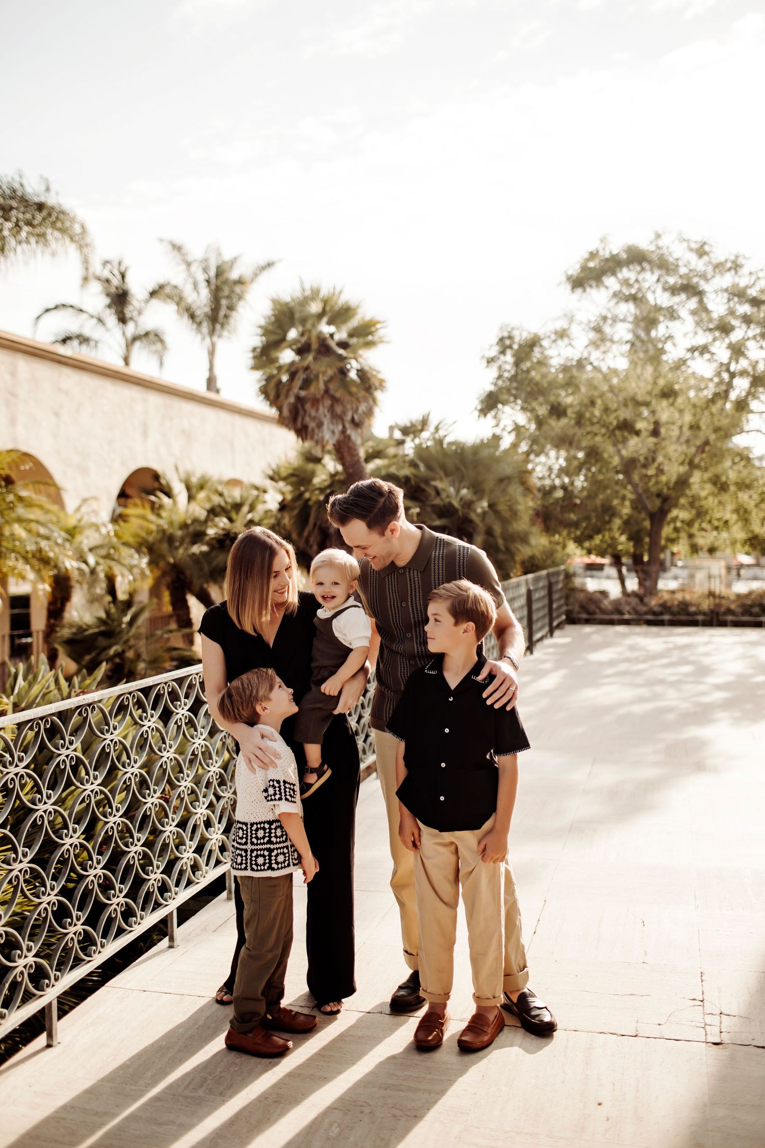 A family poses cuddled together in neutral clothing in front of Balboa Park's Timken museum.