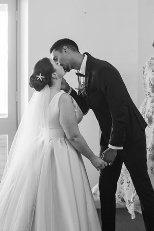A romantic black and white wedding photo of a couple sharing their first kiss as newlyweds.