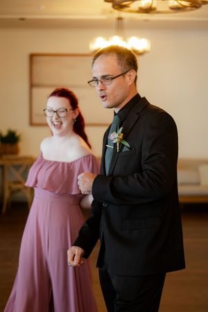 Wedding party members share joyful moments in formal attire at an indoor reception venue.