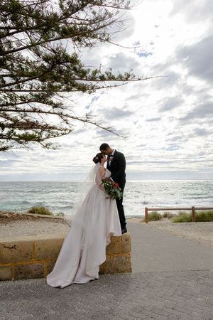 Couple sharing a romantic moment at a coastal lookout with dramatic cloudy sky and ocean views.