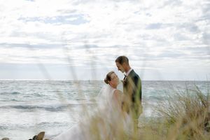 Wedding couple poses against dramatic ocean backdrop with cloudy skies and coastal vegetation.