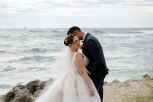 Romantic wedding photos taken on a beach with crashing waves against a rugged coastline.
