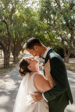 A romantic wedding couple sharing intimate kisses under tree-lined paths in an outdoor garden setting.