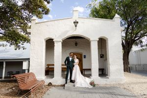 White stucco mission-style building with arched doorways and windows surrounded by trees.