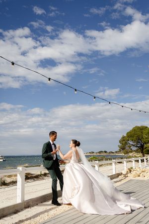 Elegant wedding photos on white deck overlooking ocean with string lights and blue sky backdrop.