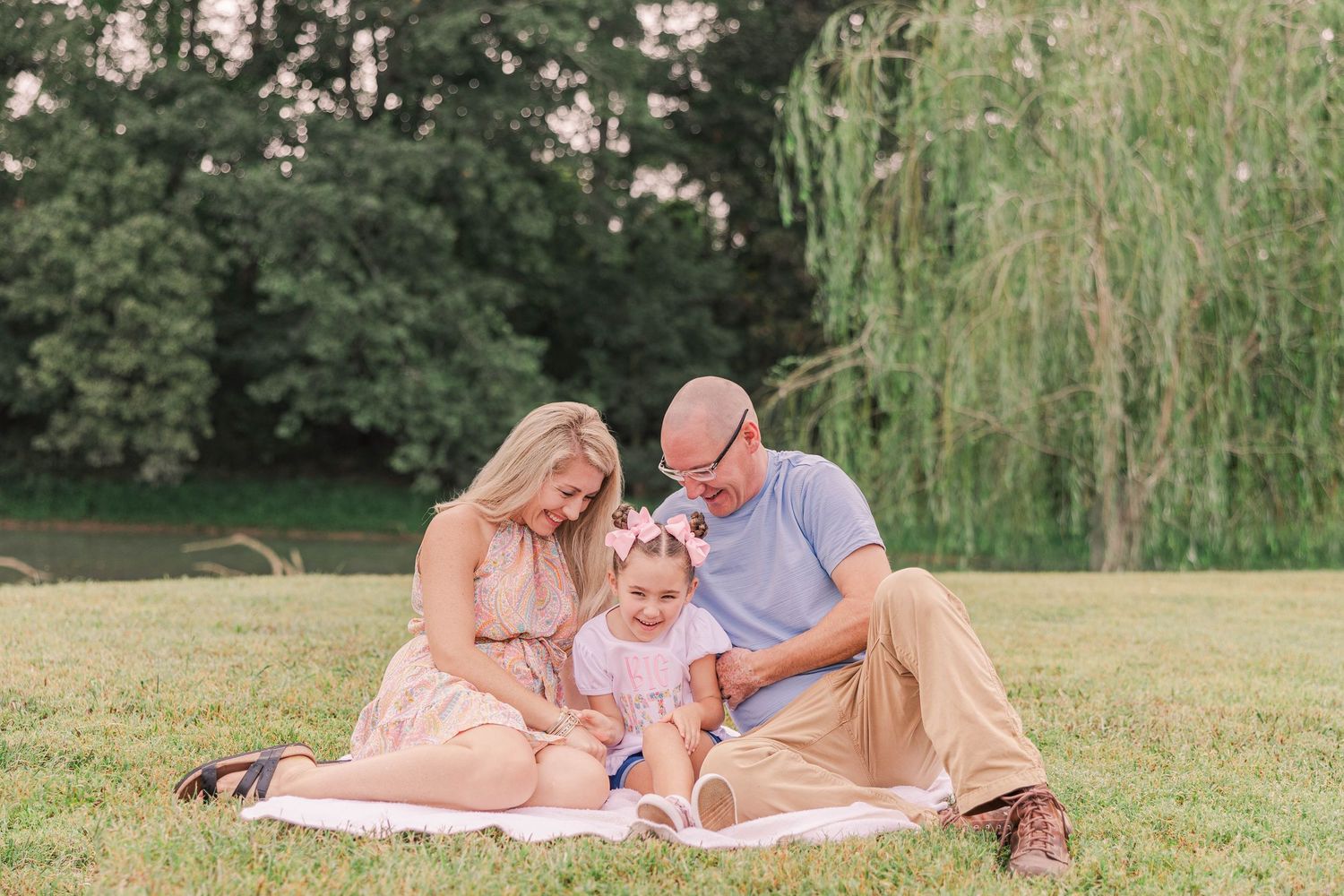 A family enjoys quality time together on a picnic blanket under weeping willow trees.