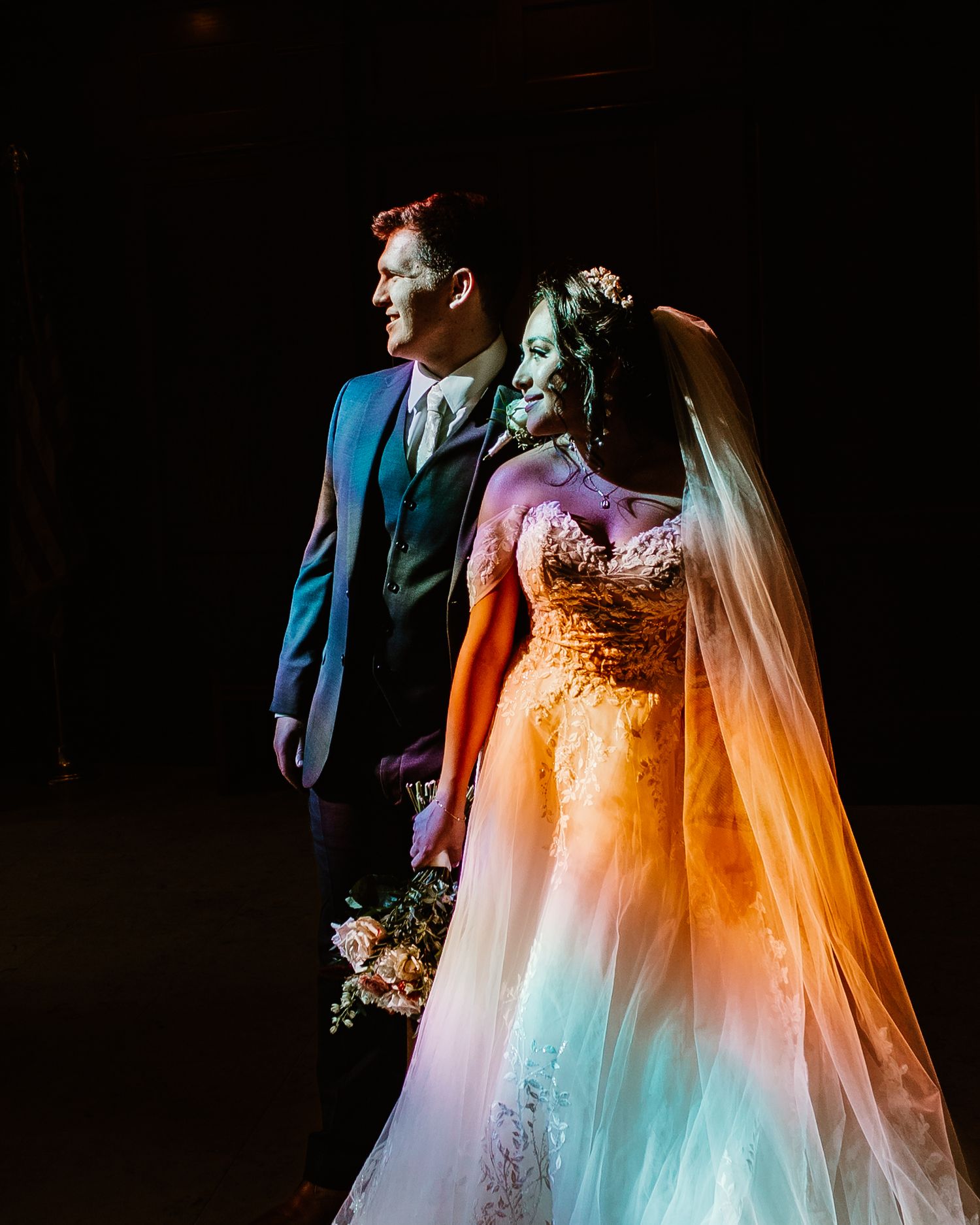Artistic wedding portrait with colorful lighting creating ethereal effect on bride's gown.