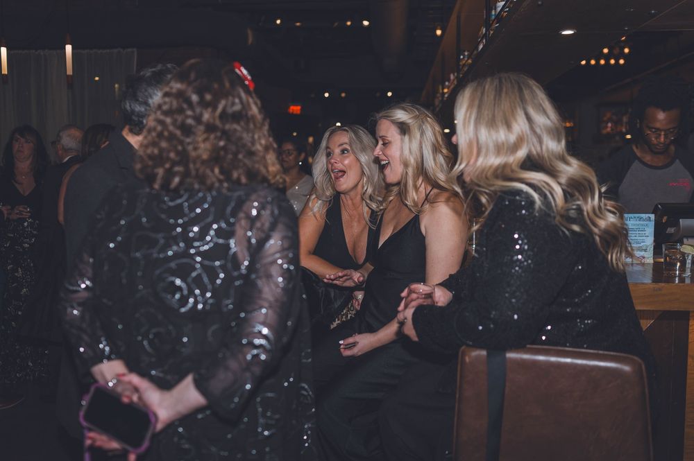 A group of people in sparkly dresses socialize at a dimly lit party or nightclub venue.