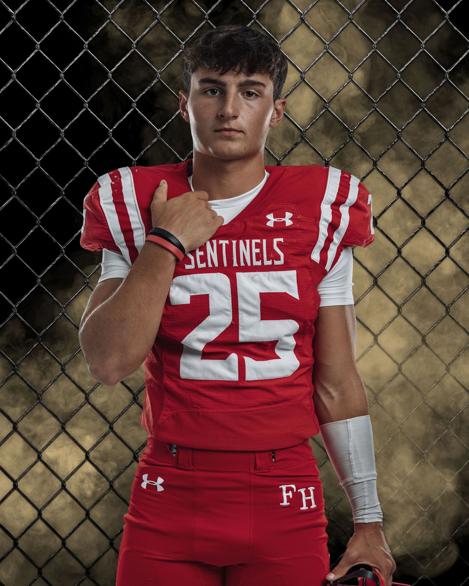 High school football players in red and white Sentinels uniforms pose against chain link fence.