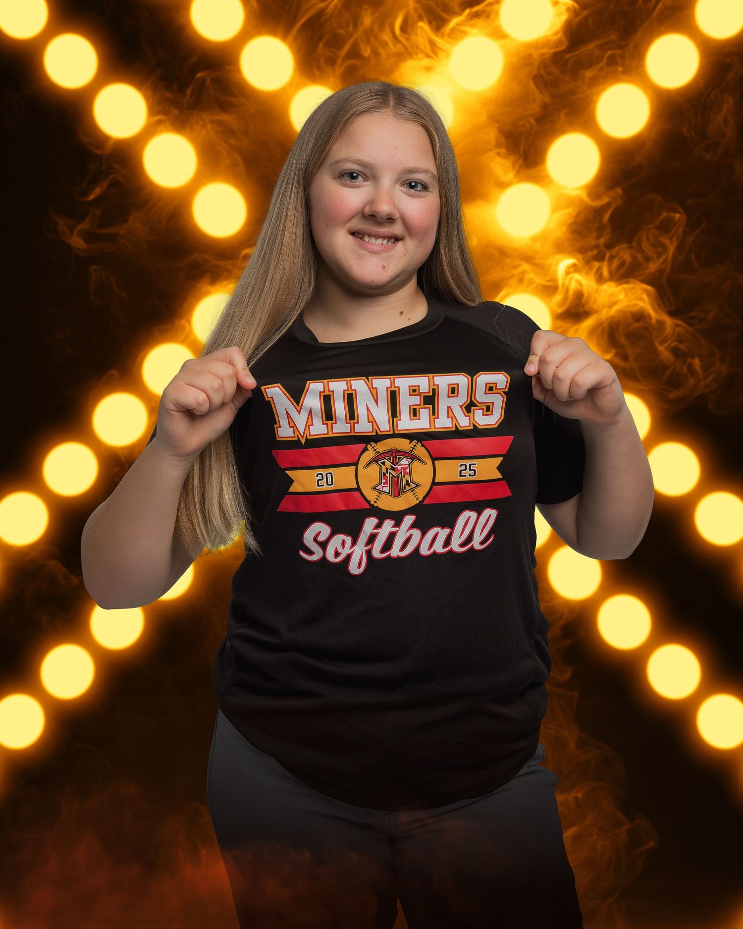 Student wearing Miners Softball t-shirt poses against glowing bokeh background.