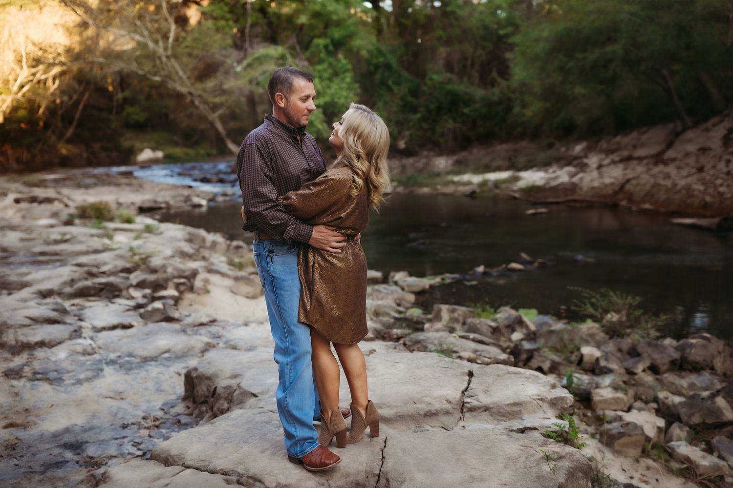 Person walks along rocky riverbed during autumn surrounded by scenic woodland and flowing water.