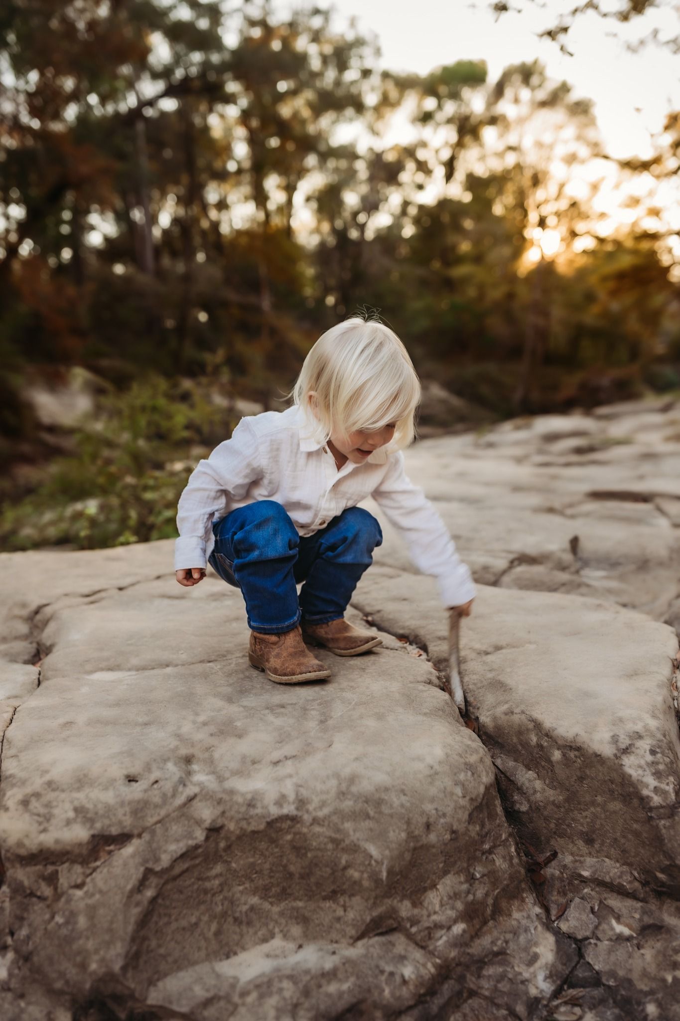 Adventurous child exploring rocky terrain at sunset while wearing white shirt and blue pants.