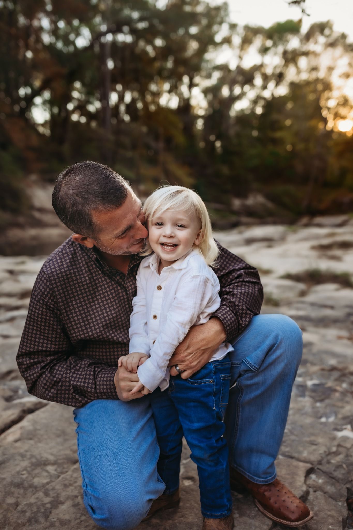 A tender moment shared in nature against a golden sunset on rocks surrounded by autumn foliage.