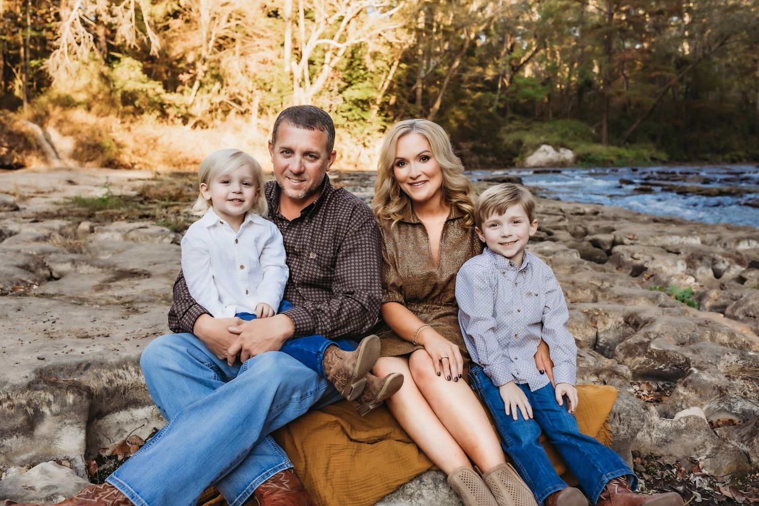 A family sits together on rocky terrain beside a flowing stream during a golden autumn afternoon.