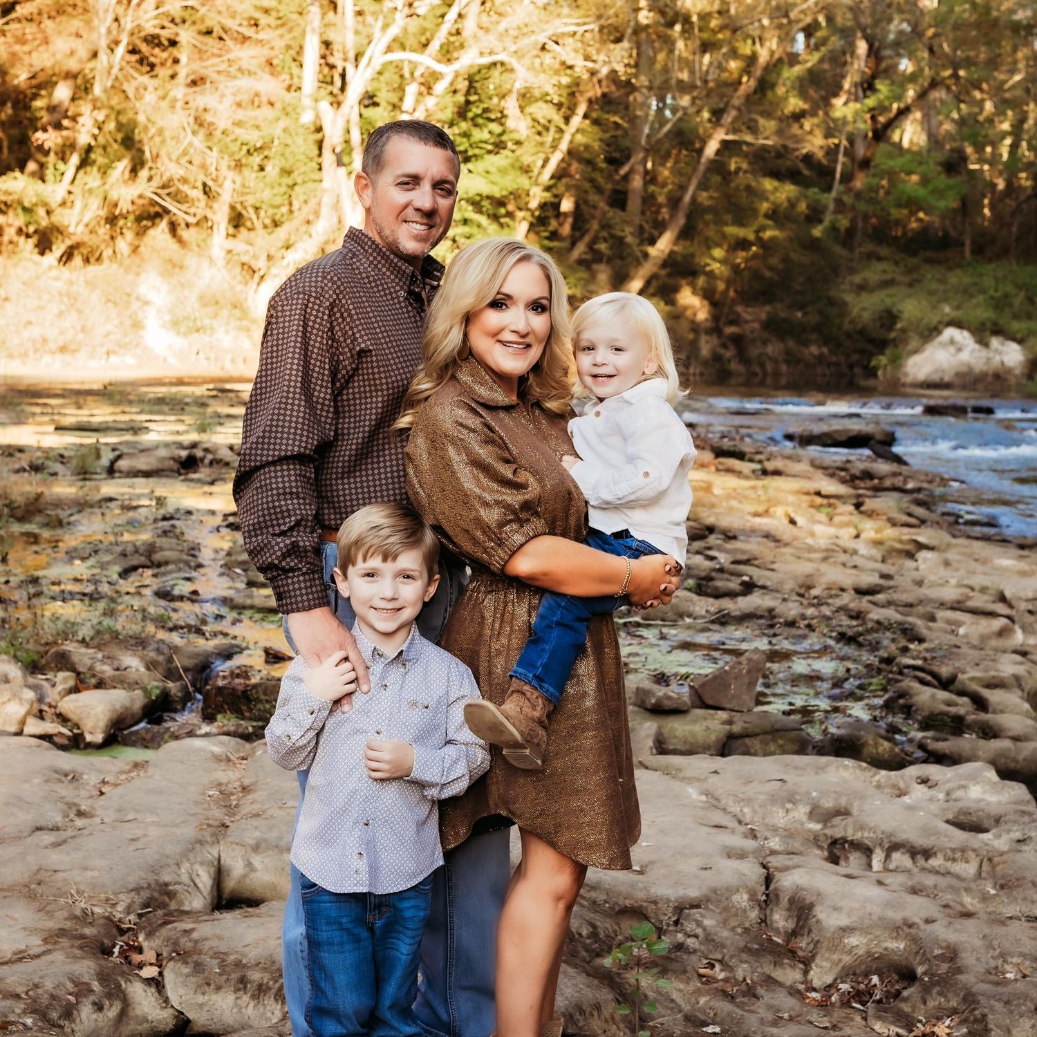 A family stands together on rocky terrain near a stream in an autumn outdoor setting.