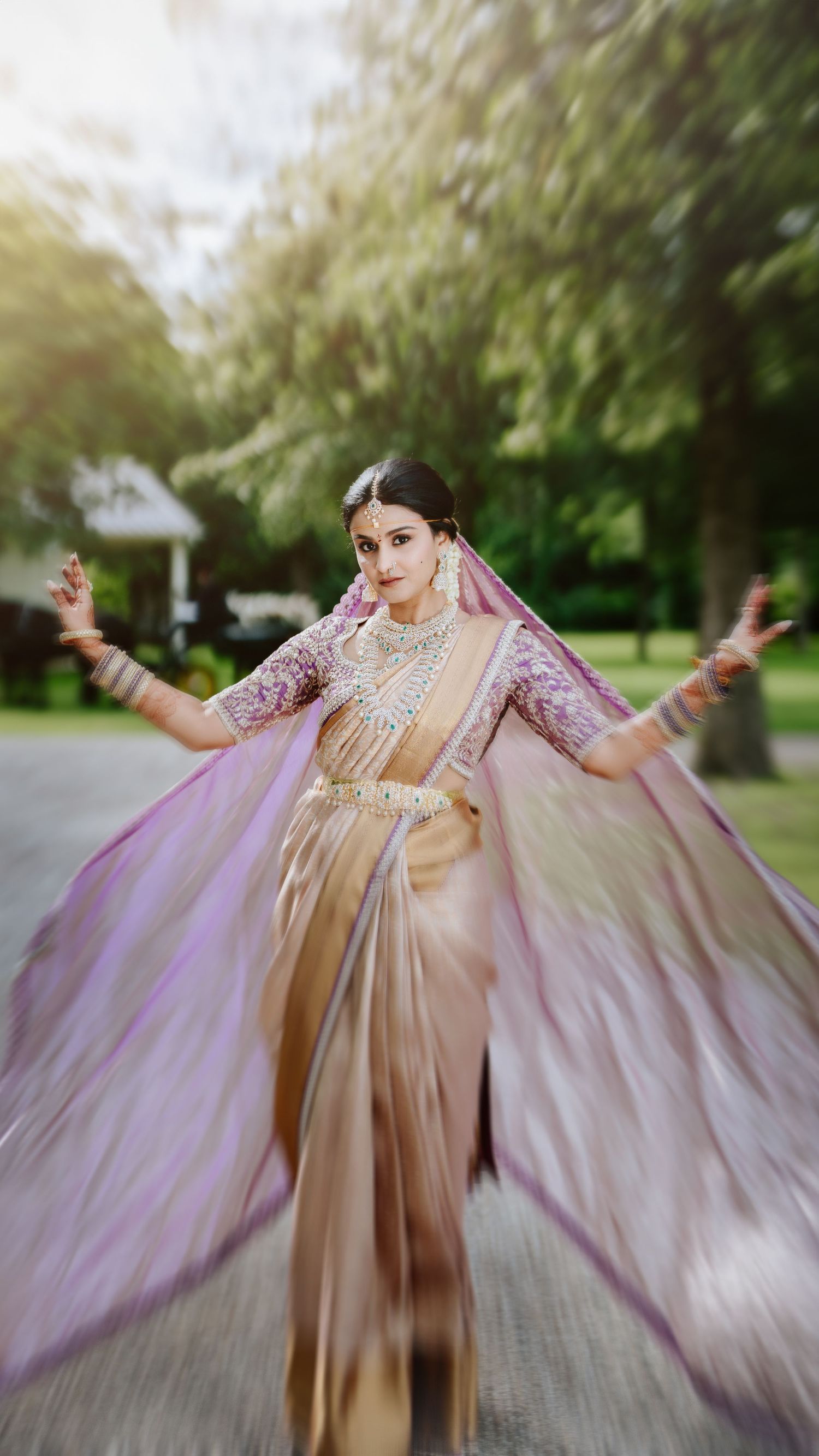 A graceful dancer in a flowing gold and lavender fusion dress spins outdoors with arms outstretched in an ethereal pose.