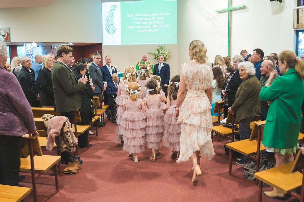 Group of people seated in church pews attending a formal ceremony with flowing pink dresses visible in multiple shots.