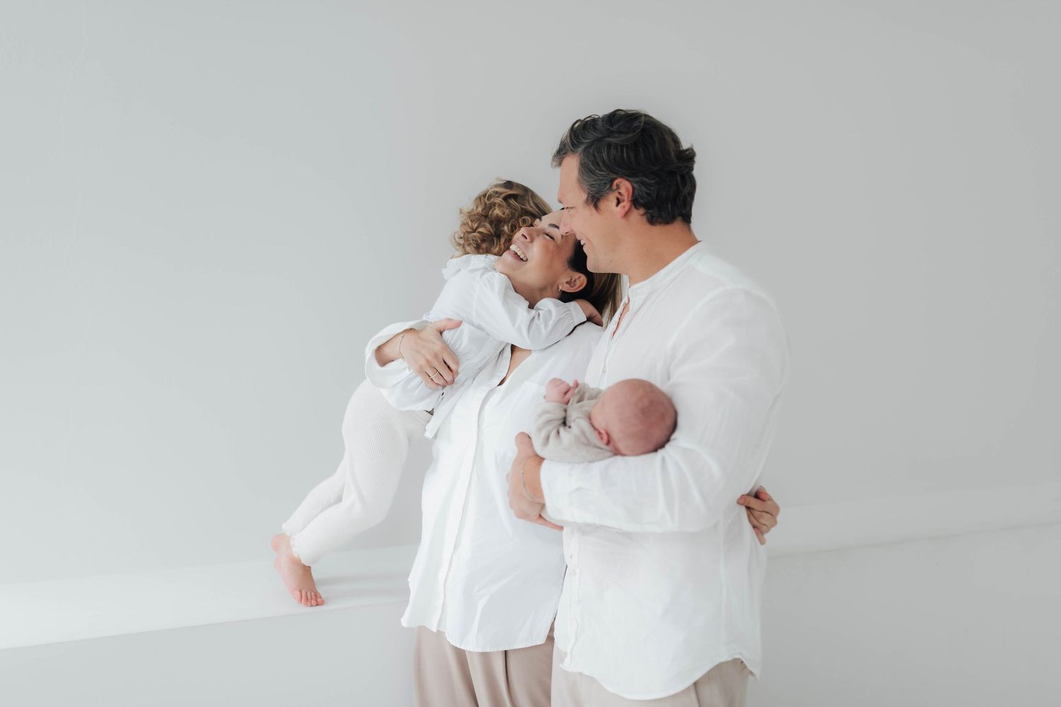 Joyful family moment on white couch as baby laughs while parents share quality time together at home.
