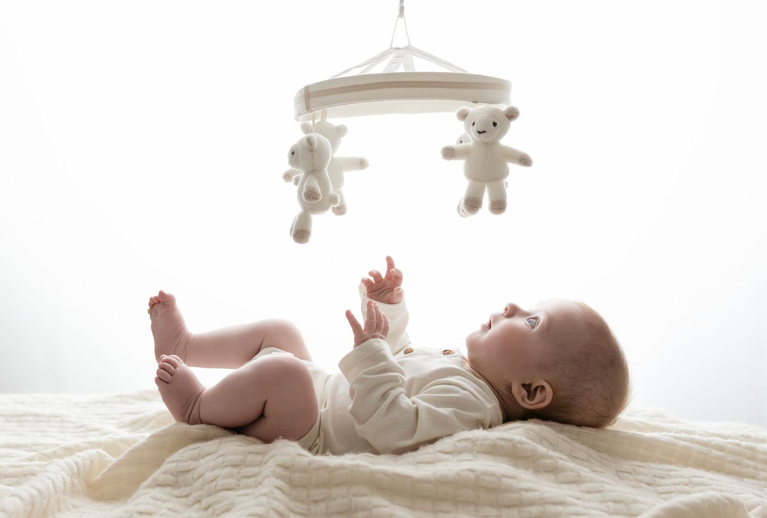 Baby girl plays with a mobile against a neutral background during her three-month milestone session with Charlottesville baby photographer.