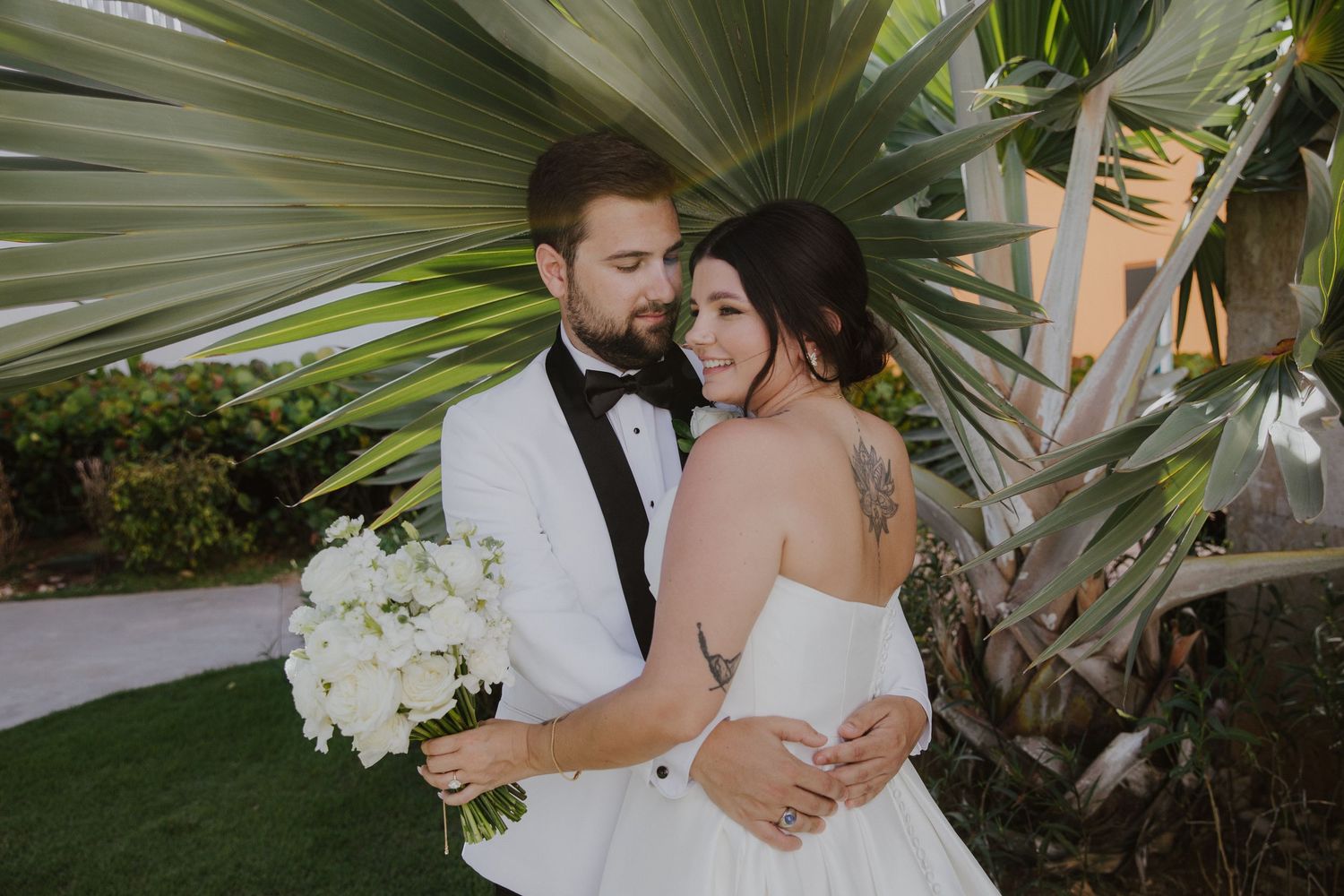 A romantic wedding portrait with the couple embracing beneath palm fronds.